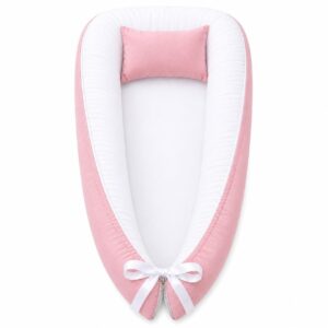 Pink outside and white inside baby nest with padded raised sides and a small matching head pillow, designed to create a cozy, secure sleeping space for infants.