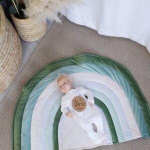 Green rainbow-shaped baby playmat in soft earthy tones, perfect for tummy time and nursery décor by Cinnamon and Spice Baby Boutique.
